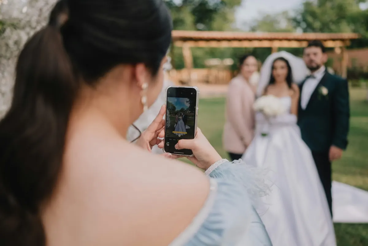 A bridesmaid framing the bride and groom on her phone