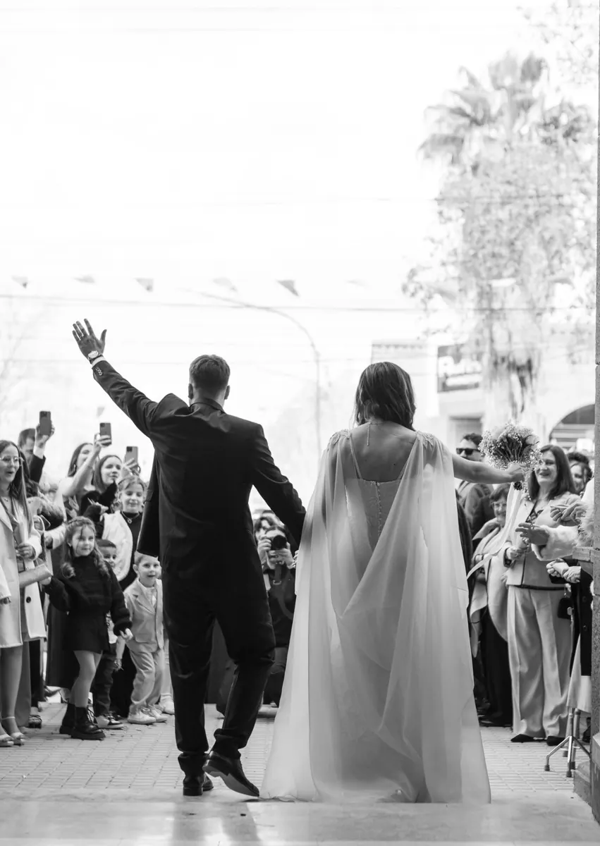 A bride and groom waving to cheering guests as they leave the church