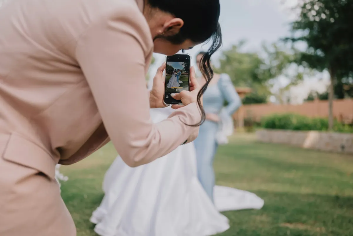 A wedding guest crouching to photograph the bride and a bridesmaid